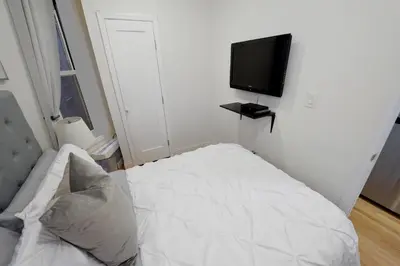 a small bedroom with a white bed and a flat screen tv at Cityscape 2 Bedroom Unit Prime Location in New York