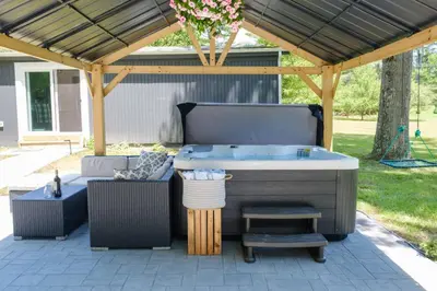 a patio with a hot tub and a pergola at Gilded Cage Escapes - Hidden Playroom For Couples - Private Hot Tub - Mountain Views - Riverfront in Lackawaxen
