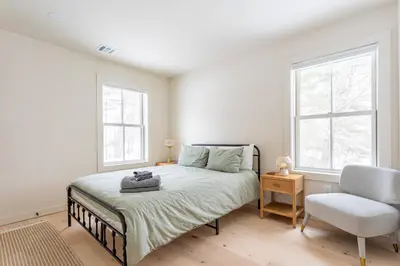 a bedroom with a bed and a chair and two windows at Lakefront Cabin with Private Dock Kenoza Den in Jeffersonville