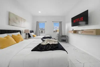 a white bedroom with two beds and a tv on the wall at 5 beds 7 person Prime Location Near Transit NYC in Jersey City