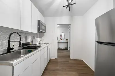 a kitchen with white cabinets and a sink and a hallway at Modern 2BR Apartment - 15 min to NYC - Sleeps 6 in West New York