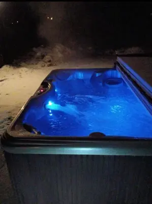 a blue hot tub in the snow at night at Huge house with Game Room, Hot Tub, 3 living rooms, 2 bonus rooms in Albrightsville