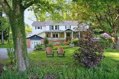 a white house with two chairs in the yard at Creekside Farmstead - Pool - Hot Tub - 3 Min to Lake - Pets Allowed in Auburn