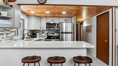 a kitchen with a large white counter and two stools at Evergreen Lodge by AvantStay Poconos Lake Cabin Fireplace Large Deck Near Jack Frost Kalahari in Locust Lakes Village