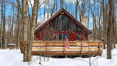a red cabin in the woods in the snow at Evergreen Lodge by AvantStay Poconos Lake Cabin Fireplace Large Deck Near Jack Frost Kalahari in Locust Lakes Village
