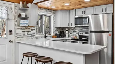 a kitchen with white cabinets and a stainless steel refrigerator at Evergreen Lodge by AvantStay Poconos Lake Cabin Fireplace Large Deck Near Jack Frost Kalahari in Locust Lakes Village