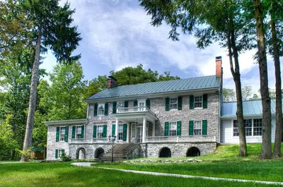 a large stone house with a porch and trees at Stocks Manor Bed and Breakfast in Mechanicsburg