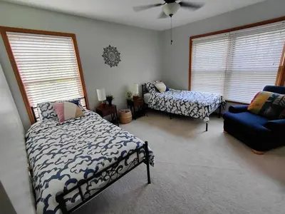 a bedroom with a bed and a chair and windows at Charming Family Friendly House, Hot tub, Playroom in Long Pond