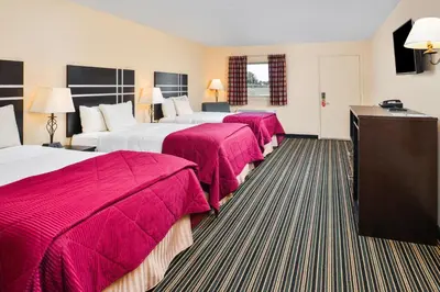 a hotel room with three beds with red sheets at Soudersburg Inn & Suites Lancaster in Ronks