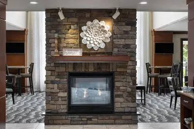 a stone fireplace in a lobby with chairs and tables at Staybridge Suites Harrisburg-Hershey by IHG in Harrisburg