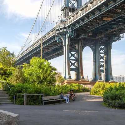 two people sitting on benches under a bridge at 1 Hotel Brooklyn Bridge in Brooklyn