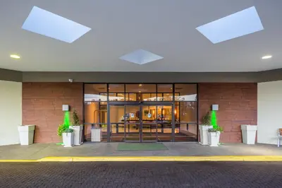 a building with glass doors and plants in front of it at Holiday Inn Philadelphia South-Swedesboro by IHG in Swedesboro