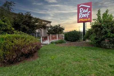 a red roof plus sign in front of a house at Red Roof PLUS Woodbridge - Carteret in Carteret