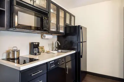 a kitchen with black cabinets and a black refrigerator at Sonesta Simply Suites Parsippany Morris Plains in Morris Plains