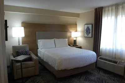 a hotel room with a bed and a chair at Candlewood Suites Harrisburg I-81 Hershey Area by IHG in Harrisburg