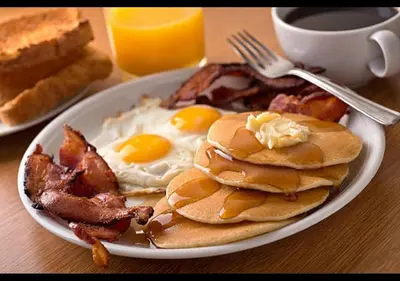 a plate of pancakes with eggs and bacon on a table at Holiday Inn Binghamton-Downtown Hawley Street by IHG in Binghamton