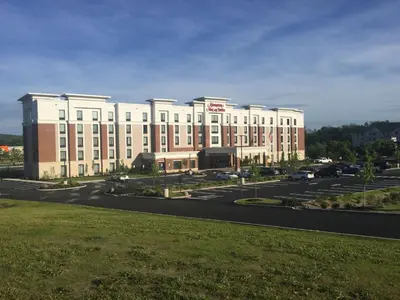a large white building with a parking lot at Hampton Inn & Suites Newburgh Stewart Airport, NY in Newburgh