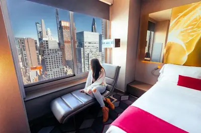 a woman sitting in a chair in a hotel room looking out the window at W New York - Times Square in New York