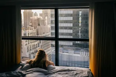 a woman laying in bed looking out of a window at Renaissance New York Times Square by Marriott in New York
