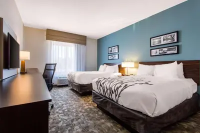 a hotel room with two beds and a desk at Sleep Inn & Suites Middletown - Goshen in Middletown