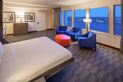 a hotel room with a bed and chairs and a large window at Hilton Philadelphia at Penn's Landing in Philadelphia