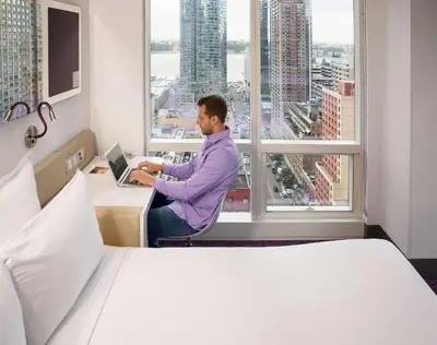 a man sitting at a desk with a laptop in front of a window at YOTEL New York Times Square in New York