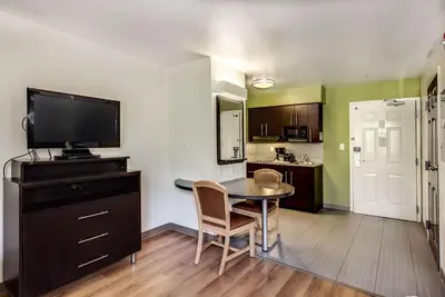 a living room with a table and a tv and a kitchen at Studio 6-East Brunswick, NJ - NYC Area in East Brunswick