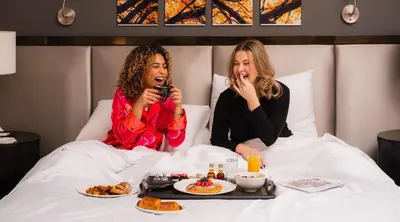 two women sitting in bed taking pictures of food at Royalton Park Avenue in New York