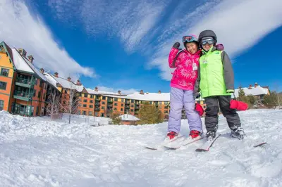 two children on skis in the snow in front of a hotel at The Appalachian at Mountain Creek in Vernon