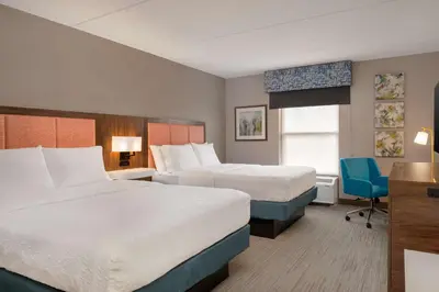 a hotel room with two beds and a blue chair at Hampton Inn Bloomsburg in Bloomsburg