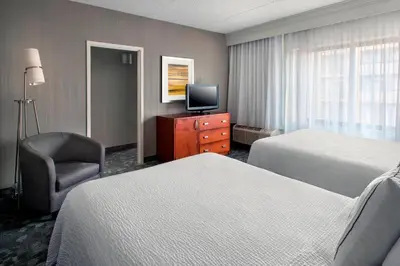a hotel room with two beds and a chair and a television at Courtyard Newark Liberty International Airport in Newark