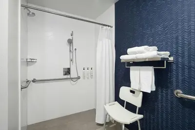 a bathroom with a shower and a white chair at Fairfield Inn & Suites by Marriott Newark Liberty International Airport in Newark