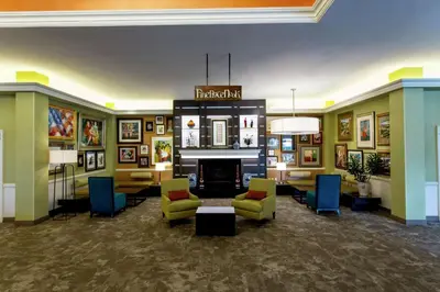 a lobby with a fireplace and chairs and paintings at Hilton Garden Inn New York/Staten Island in Staten Island