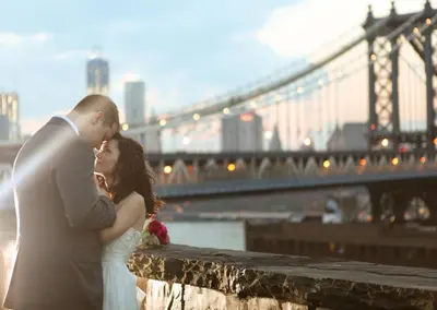 a bride and groom kissing in front of a bridge at M Social Hotel New York Downtown in New York