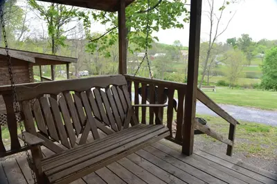 a wooden bench on a porch with a swing at Robin Hill Camping Resort One-Bedroom Cottage 8 in Lenhartsville