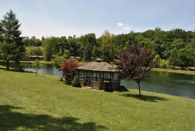 a gazebo in the grass next to a lake at Robin Hill Camping Resort Premium Cottage 9 in Lenhartsville