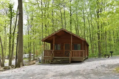 a small wooden cabin in the woods with a picnic table at Sun Valley Campground Cottage 6 in Maple Grove Park