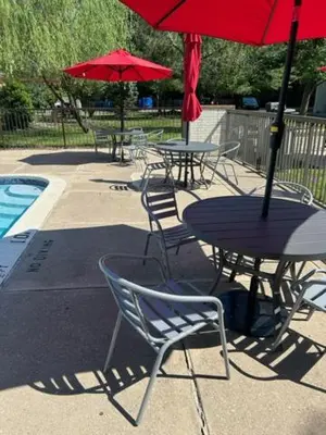 a table and chairs with red umbrellas next to a pool at Ramada by Wyndham Newark/Wilmington in Newark