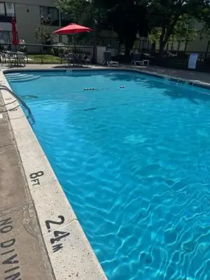 a large blue swimming pool with a red umbrella at Ramada by Wyndham Newark/Wilmington in Newark