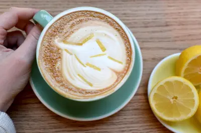 a person holding a cup of cappuccino next to lemon slices at Freehand New York in New York