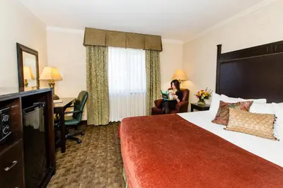 a hotel room with a bed and a woman sitting in a chair at Heritage Hotel Lancaster in Lancaster