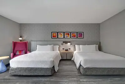 a bedroom with two beds and a red chair at Hilton Garden Inn Hamilton in Bordentown