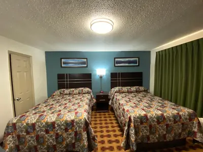 two beds in a hotel room with green curtains at Lodge Inn Wrightstown - Fort Dix in Wrightstown