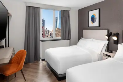 a hotel room with two beds and a desk and a window at voco Times Square South New York by IHG in New York