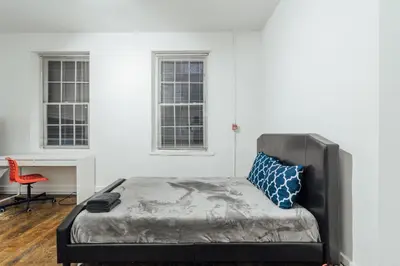 a bed in a room with a red chair and two windows at The Havana Lofts in Philadelphia