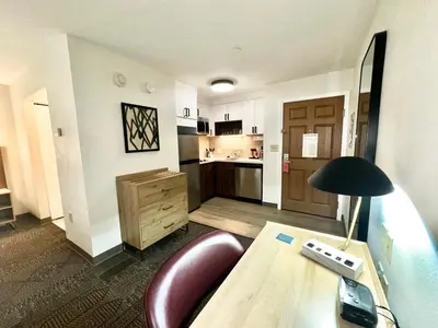 a room with a desk with a lamp and a kitchen at Staybridge Suites East Stroudsburg - Poconos by IHG in East Stroudsburg