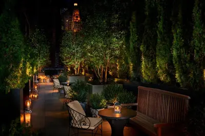 a patio with tables and chairs and trees at night at The Times Square EDITION New York in New York