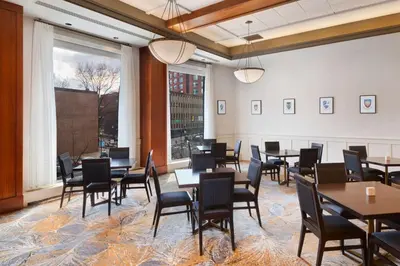 a dining room with tables and chairs and a large window at The Inn at Penn, A Hilton Hotel in Philadelphia