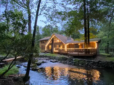 a house in the woods with a river in front of it at Secluded Greekside Cabin near Camelback in Tannersville