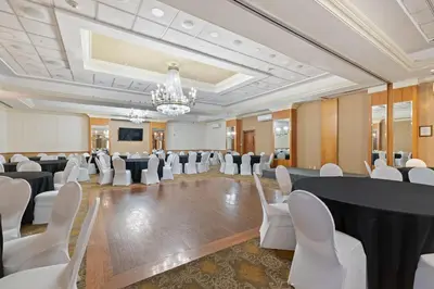 a banquet hall with white chairs and tables and a chandelier at Hotel Executive Suites in Carteret